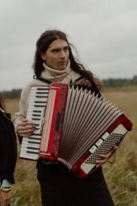 Man with turtleneck playing accordion in open field.