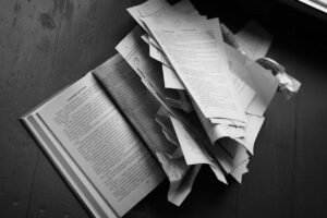 Dramatic black and white image of torn book pages scattered over a wooden floor.